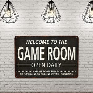 May include: A black and white metal sign with the text "Welcome to the Game Room Open Daily" and the rules "Game Room Rules: No Cursing, No Fighting, No Spitting, No Whining".