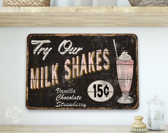 Peut inclure: Une enseigne en bois de style vintage avec un fond noir et du texte blanc qui dit "Try Our Milk Shakes". L'enseigne présente également un dessin d'un milk-shake avec une paille et une étiquette de prix qui indique "15¢". L'enseigne liste les saveurs "Vanilla, Chocolate, Strawberry".