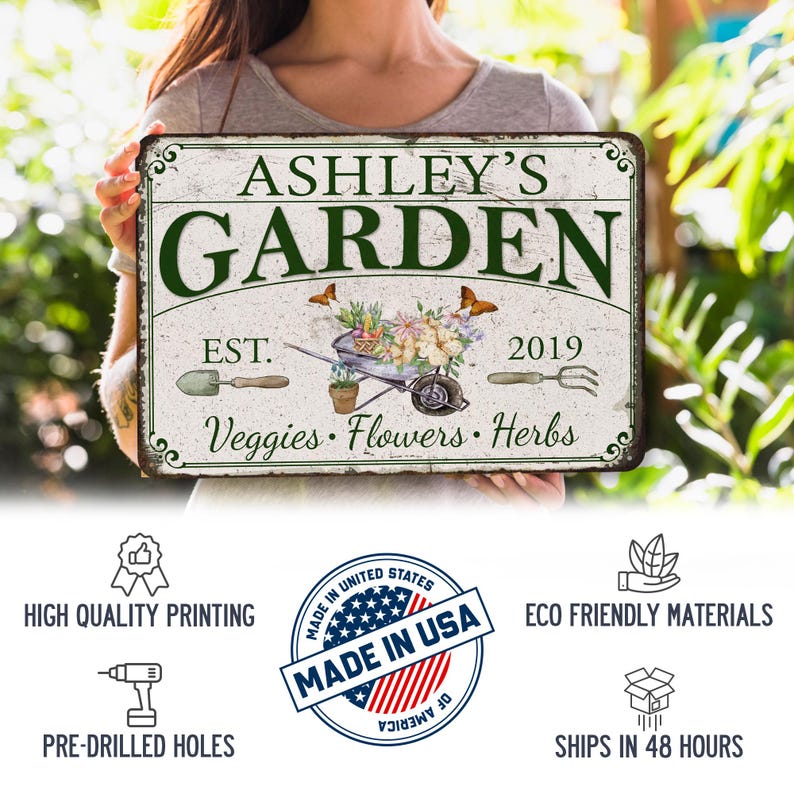 Peut inclure: Une plaque en m&eacute;tal blanc avec une finition vieillie comportant le texte "Ashley's Garden" en lettres vertes. La plaque comprend &eacute;galement le texte "Est. 2019" et "L&eacute;gumes, Fleurs, Herbes".