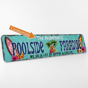 Pode incluir: Uma placa de metal azul turquesa e branco com o texto "Poolside Paradise" em letras azuis. A placa tamb&eacute;m apresenta uma palmeira, flores e uma prancha de surf. O texto "The Anderson's" est&aacute; acima do texto principal e o texto "We do a lot of sippin' & chillin'" est&aacute; abaixo do texto principal.