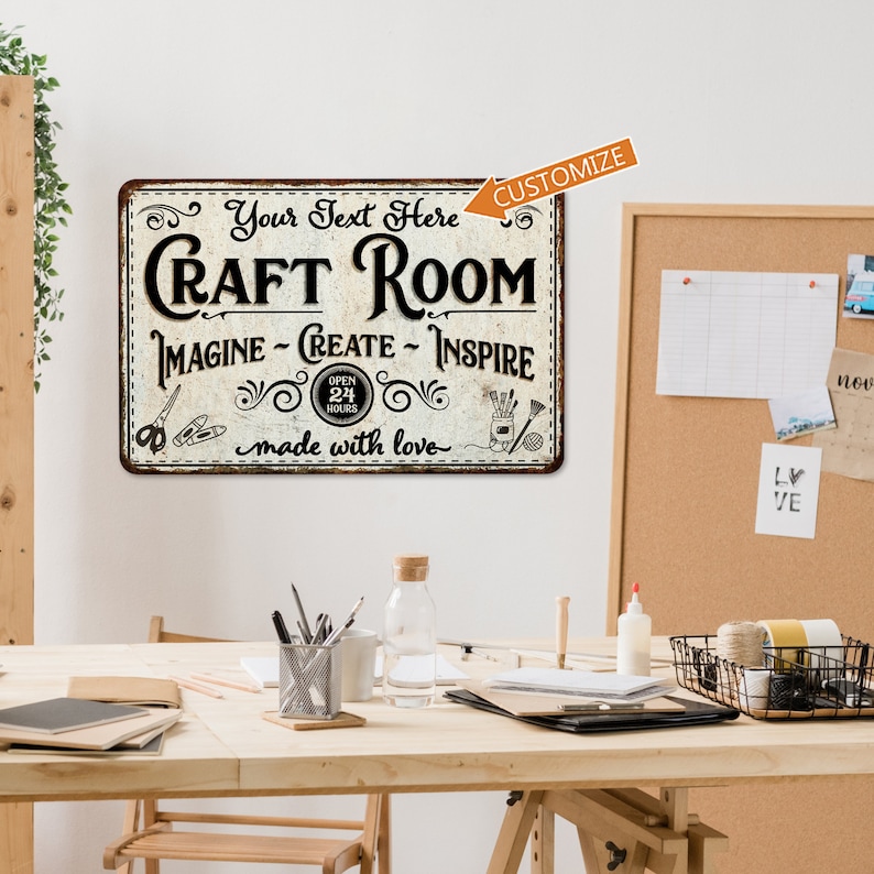 May include: A vintage-style metal sign with a white background and black text that reads "Craft Room" with the words "Imagine - Create - Inspire" below. The sign also includes a small image of an open clock with the words "Open 24 Hours" and a small image of a craft supply basket. The sign has a distressed look and the words "made with love" are written below the main text.