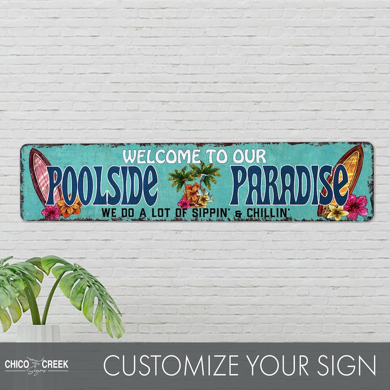 Pode incluir: Uma placa de metal azul turquesa com o texto "Welcome to our Poolside Paradise We do a lot of sippin' & chillin'" em branco. A placa apresenta duas pranchas de surf com flores tropicais e palmeiras.