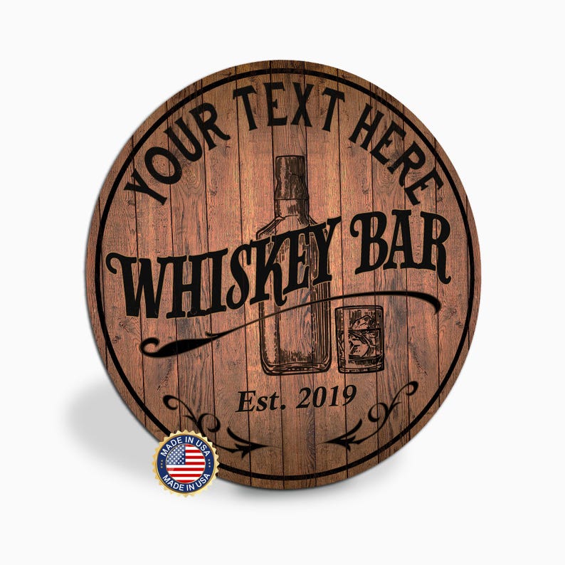 May include: Round wooden sign with a whiskey bar theme. The sign features the text "YOUR TEXT HERE" at the top, "WHISKEY BAR" in the center, and "Est. 2019" at the bottom. A whiskey bottle and glass are illustrated in the center. Includes a "Made in USA" sticker.