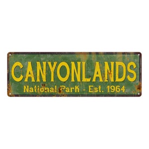 May include: A vintage-style metal sign with a green background and yellow text that reads "Canyonlands National Park - Est. 1964". The sign has a rusty appearance.
