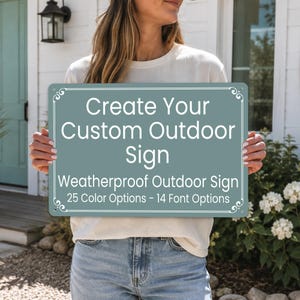 May include: A rectangular, sage green outdoor sign with white text that reads: Create Your Custom Outdoor Sign, Weatherproof Outdoor Sign, 25 Color Options - 14 Font Options. The sign features a thin white border with decorative corner flourishes.