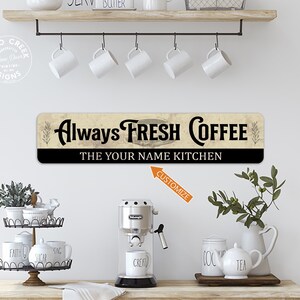 May include: A rustic wooden sign with black lettering that reads "Always Fresh Coffee The YOUR NAME Kitchen". The sign has a distressed, vintage look and is perfect for a kitchen or coffee bar.