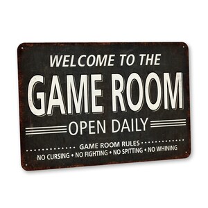 May include: A black and white metal sign with the text "Welcome to the Game Room Open Daily" and the rules "Game Room Rules: No Cursing, No Fighting, No Spitting, No Whining".