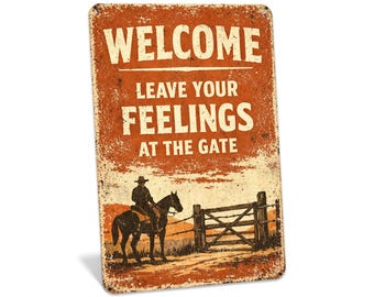 Könnte beinhalten: Rechteckiges Metallschild im Vintage-Stil mit orangefarbenem Hintergrund und weißem Text, der lautet: "WELCOME LEAVE YOUR FEELINGS AT THE GATE". Ein Cowboy auf einem Pferd ist in der Nähe eines hölzernen Tores abgebildet.