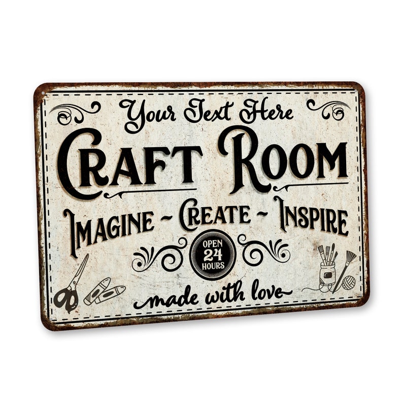 May include: A vintage-style metal sign with a distressed white background and black text that reads "Your Text Here Craft Room Imagine - Create - Inspire Open 24 Hours made with love". The sign features decorative swirls and images of scissors, pencils, paintbrushes, and yarn.