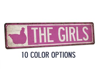 May include: A pink metal sign with a silhouette of a chicken and the text "THE GIRLS" in white. The sign has a distressed, vintage look. 10 color options are available.