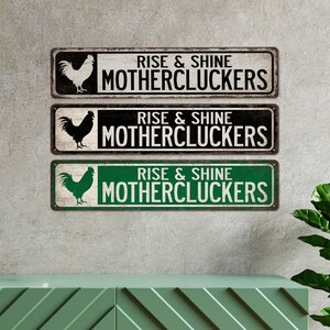 May include: Three metal signs featuring a rooster silhouette and the text "Rise & Shine Mothercluckers". The signs are in black and white, black and white with a distressed look, and green and white.