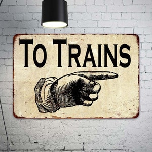 May include: A vintage-style metal sign with a distressed background. The sign reads "TO TRAINS" in black lettering with a pointing hand graphic.