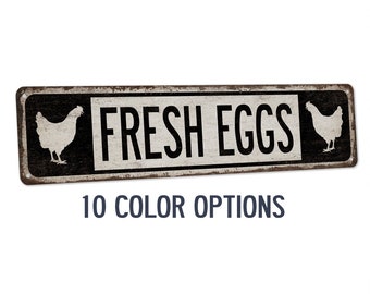May include: A black and white metal sign with a distressed look. The sign reads "FRESH EGGS" with a white silhouette of a chicken on each side. The sign has a brown background and black lettering. The text "10 COLOR OPTIONS" is printed below the sign.