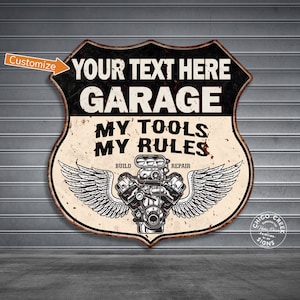 May include: A vintage-style metal sign with a black and white background. The sign features a stylized engine with wings and the text "YOUR TEXT HERE GARAGE MY TOOLS MY RULES BUILD REPAIR".