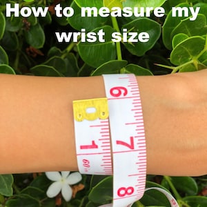 May include: A white tape measure with red markings is wrapped around a person's wrist. The tape reads 7 and 8 inches.
