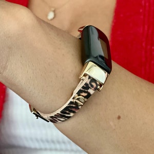 Op de afbeelding: Een zwarte fitness tracker met een gouden band en een luipaardprint.