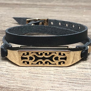 Può includere: Un braccialetto a doppio giro in pelle nera con un ciondolo in metallo dorato con un design a taglio decorativo.