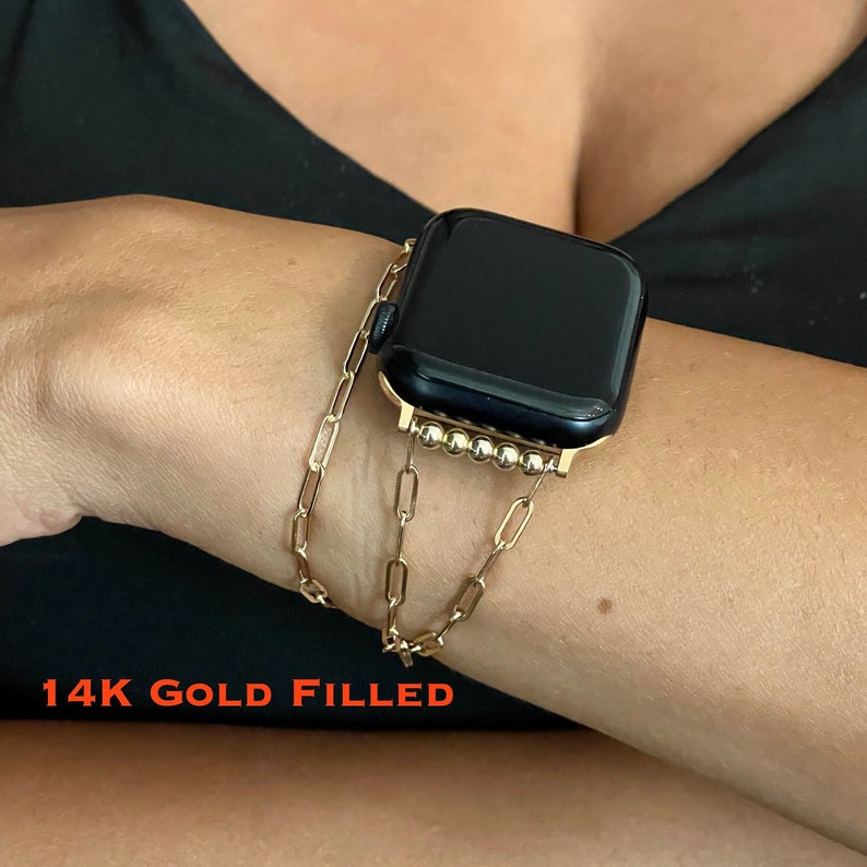 Puede incluir: Una pulsera de reloj de oro relleno con un dise&ntilde;o de eslabones de cadena. La pulsera est&aacute; hecha de metal de oro relleno de 14 quilates y tiene un detalle de cuentas alrededor de la esfera del reloj. La pulsera se muestra en la mu&ntilde;eca de una persona.