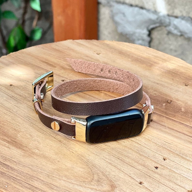 May include: A brown leather fitness tracker band with a gold buckle and a black fitness tracker