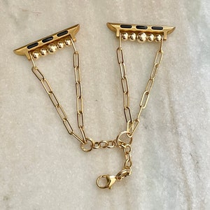 May include: A gold chain Apple Watch band with black accents and a clasp closure.