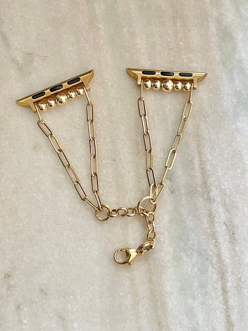 May include: A gold chain Apple Watch band with black accents and a clasp closure.