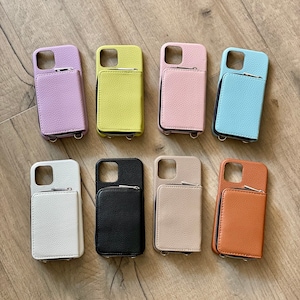 May include: Eight different colored phone cases with a small pocket on the back. The cases are made of leather and have a zipper closure. The colors are lavender, yellow, pink, light blue, white, black, beige, and brown.