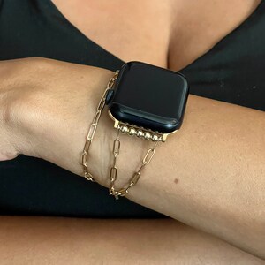 Puede incluir: Una pulsera de reloj de cadena dorada con un Apple Watch negro. La pulsera est&aacute; hecha de una cadena con peque&ntilde;as cuentas redondas.