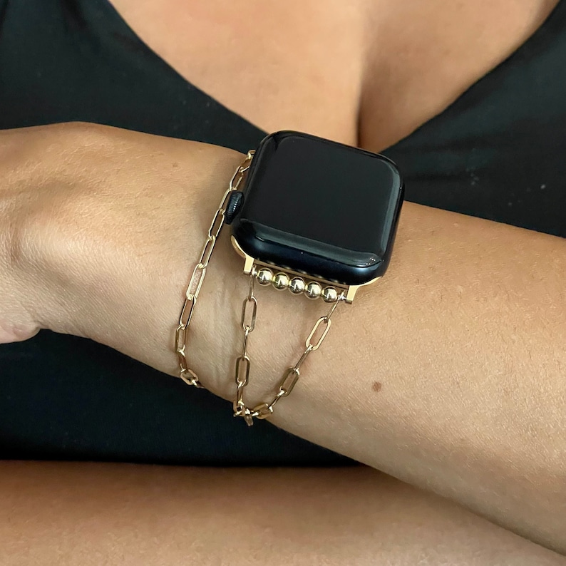 Puede incluir: Una pulsera de reloj de cadena dorada con un Apple Watch negro. La pulsera est&aacute; hecha de una cadena con peque&ntilde;as cuentas redondas.