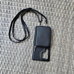 May include: Black faux leather phone case with a zippered pocket and a long black strap. The case has a clear window for the phone screen.