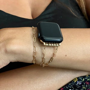 Puede incluir: Una pulsera de reloj de cadena dorada con un Apple Watch negro. La pulsera de reloj est&aacute; hecha de una cadena con peque&ntilde;as cuentas doradas.