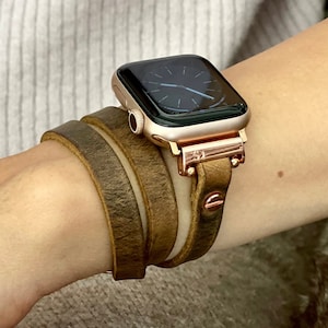 May include: A rose gold Apple Watch with a brown leather band. The band is a double wrap style and has a distressed look.