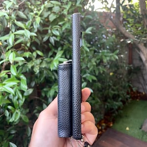 May include: Two black leather phone cases with a black strap. The cases are side by side and have a textured finish.
