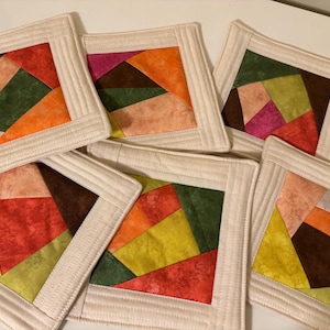 Puede incluir: Seis posavasos de tela hechos a mano con un diseño de patchwork. Cada posavasos presenta una combinación de colores diferente: naranja, amarillo, verde, marrón, rosa y rojo.