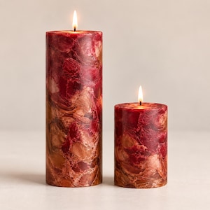 Peut inclure: Deux bougies piliers avec des flammes allumées. Les bougies ont un aspect marbré avec des nuances de rouge, de brun et d'or. Une bougie est plus haute que l'autre. Les bougies sont cylindriques et ont un style rustique et décoratif.