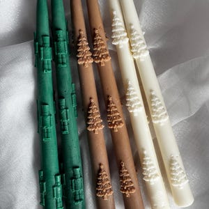 Puede incluir: Seis velas cónicas en varios colores. Dos velas verdes con un diseño geométrico, dos velas marrones con adornos de árboles de Navidad y dos velas marfil con adornos de árboles de Navidad. Cada vela tiene una mecha blanca.