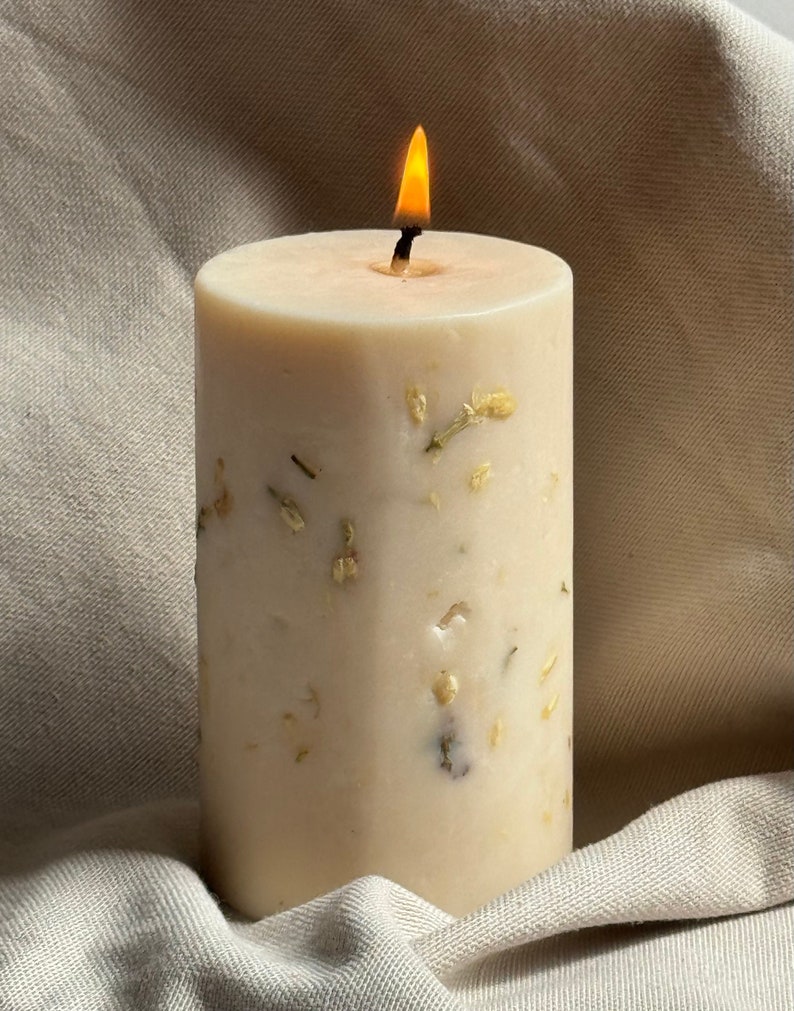 May include: A white candle with dried flowers embedded in the wax. The candle is lit and the flame is visible.