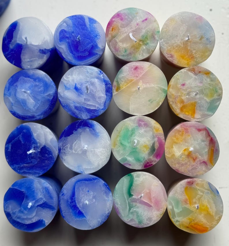 May include: A collection of sixteen round candles. The candles are arranged in a grid pattern and feature a variety of colors, including blue, green, pink, and yellow. Each candle has a small wick in the center.