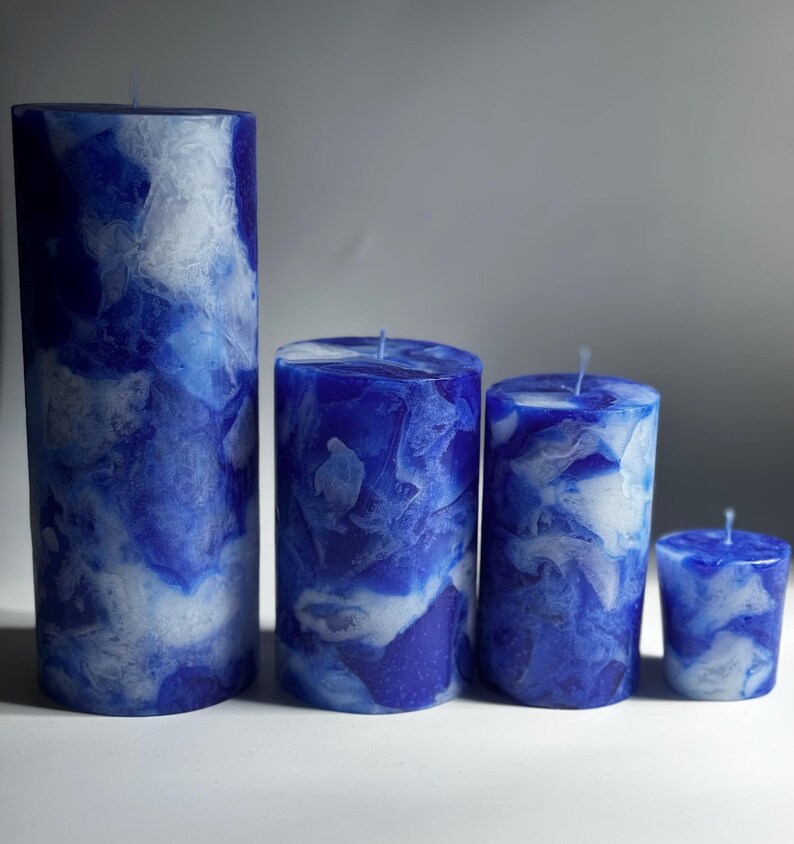 May include: Four blue pillar candles of varying heights, with a marbled white and blue design. The candles are cylindrical, with a wick at the top. The tallest candle is on the left, with the smallest on the right.