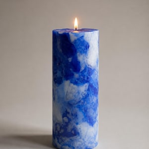 May include: A lit, cylindrical candle with a marbled blue and white design. The candle has a smooth texture and a small flame at the top. The candle is a decorative item.