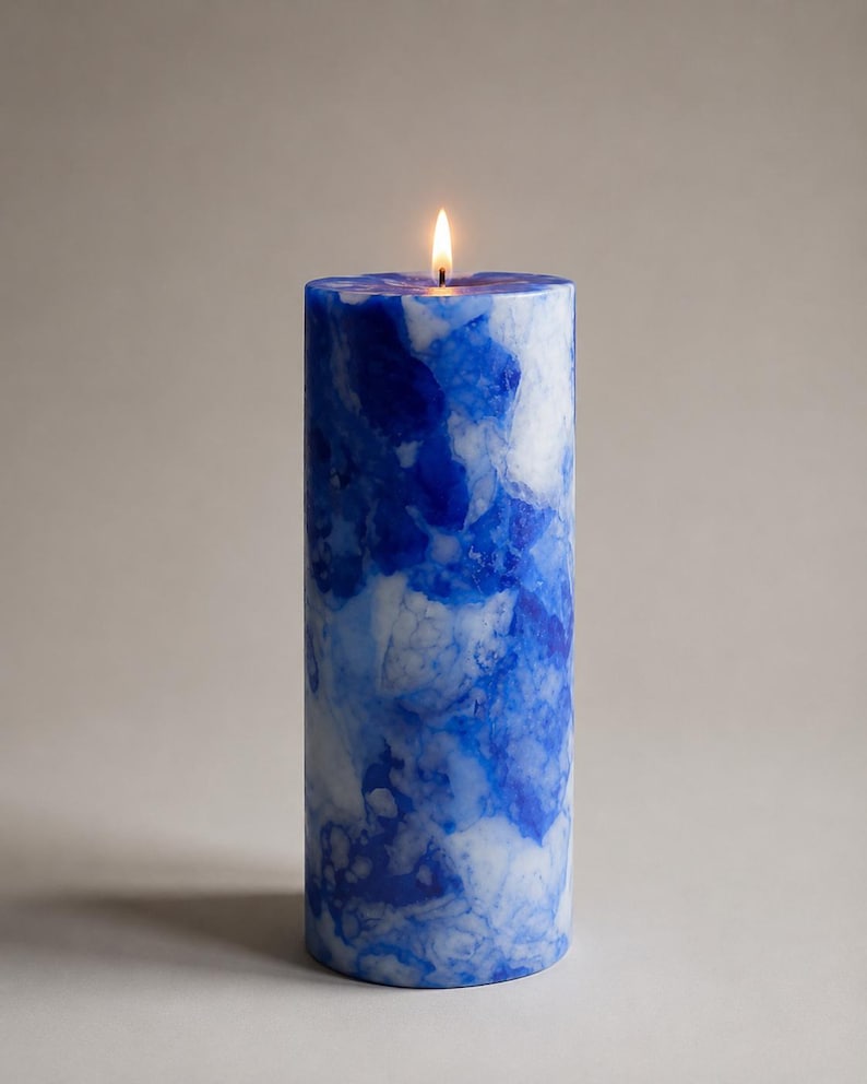 May include: A lit, cylindrical candle with a marbled blue and white design. The candle has a smooth texture and a small flame at the top. The candle is a decorative item.