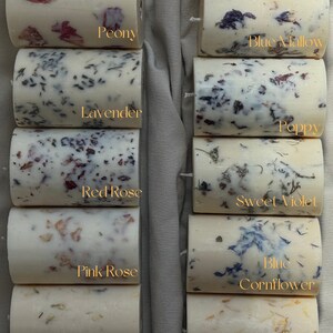 May include: Ten candles with different floral scents and dried flowers embedded in the wax. The candles are arranged in two rows of five. The flowers are visible in the wax and include sunflower, peony, blue mallow, lavender, poppy, red rose, sweet violet, pink rose, blue cornflower, jasmine, marigold, chamomile, and heather.