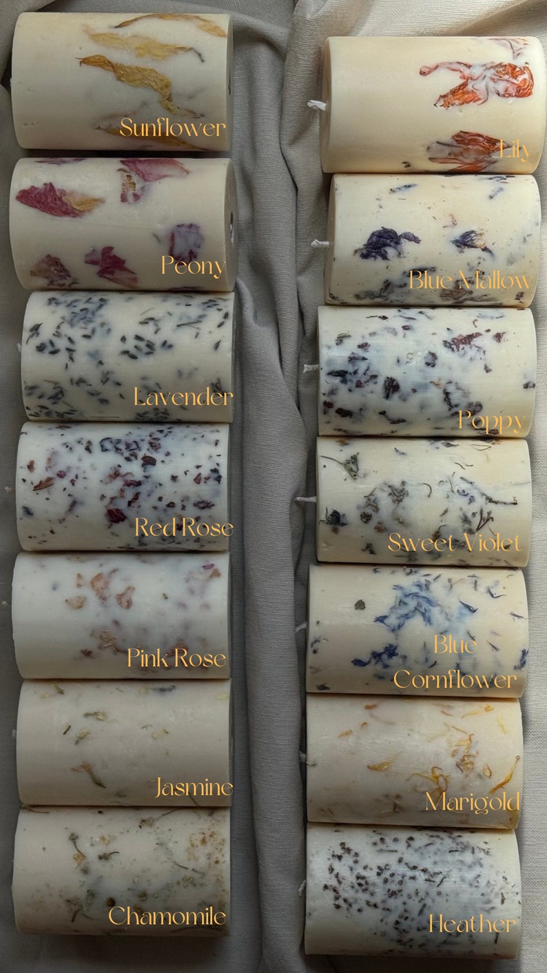 May include: Ten candles with different floral scents and dried flowers embedded in the wax. The candles are arranged in two rows of five. The flowers are visible in the wax and include sunflower, peony, blue mallow, lavender, poppy, red rose, sweet violet, pink rose, blue cornflower, jasmine, marigold, chamomile, and heather.