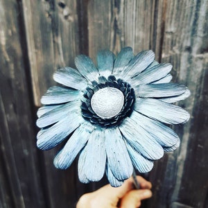 May include: A blue metal daisy flower with a silver center. The flower is made of individual metal petals and is a unique and decorative piece.
