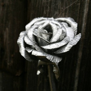 May include: A silver metal rose sculpture with a textured finish. The rose is in full bloom and has a long stem.