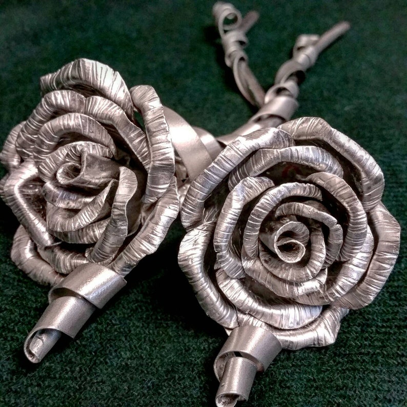 May include: Two silver metal roses with twisted stems. The roses are made of metal and have a textured surface.