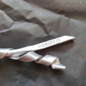 May include: A silver metal ribbon with a date stamped on it, reading "08 SEPT 11".