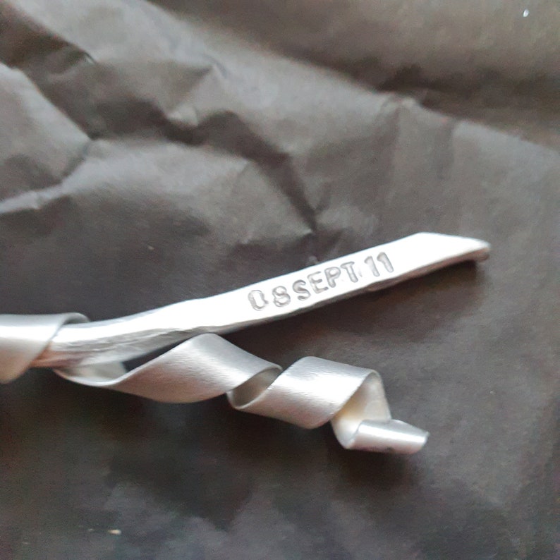 May include: A silver metal ribbon with a date stamped on it, reading "08 SEPT 11".