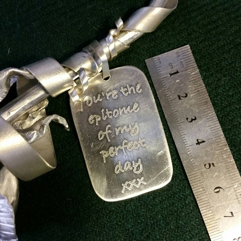 May include: A silver metal rose with a tag attached that reads "You're the epitome of my perfect day XXX". The tag is next to a ruler measuring 6 cm.