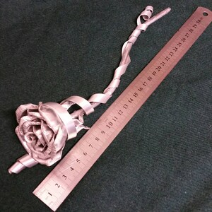 May include: A silver metal rose with a twisted stem, measuring approximately 29 inches in length. The rose is crafted from metal and has a realistic appearance.