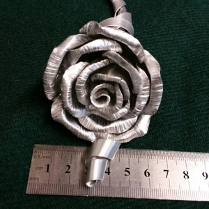 May include: A silver metal rose with a stem that is twisted and curled. The rose is about 4 inches in diameter and is measured against a ruler.